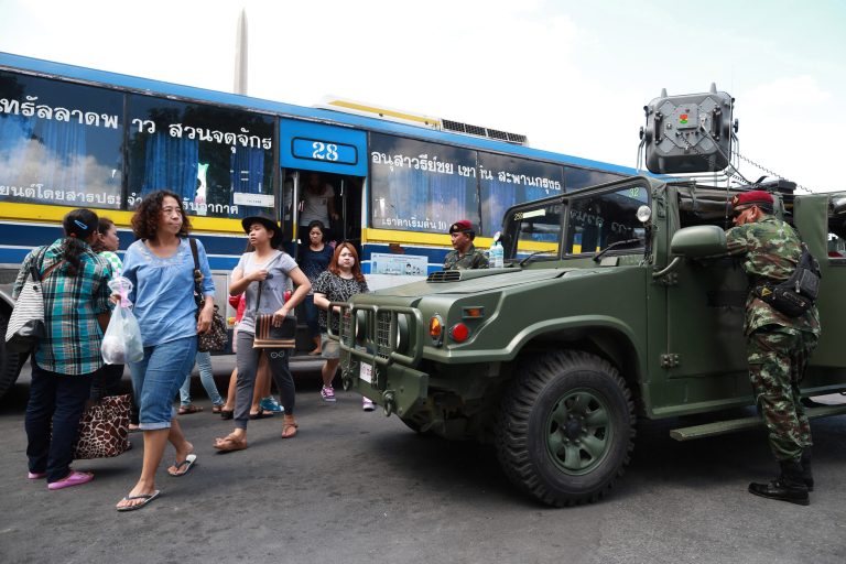 Thai soldiers stand guard near their vehicle as bus passengers walk past in Bangkok's Victory Monument, Thailand, Sunday, June 8, 2014. Thai police warned online critics of the military junta Friday that they will 