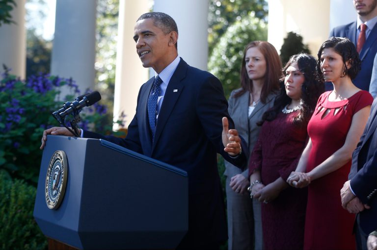 President Obama speaks about the rollout of the health care overhaul in the Rose Garden of the White House. Behind him, in a red dress, is Karmel Allison, who lost her balance while the president was speaking. (AP Photo/Charles Dharapak)