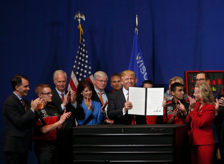 President Donald Trump holds up a signed an executive order to tighten the rules for technology companies seeking to bring highly skilled foreign workers to the U.S., Tuesday, April 18, 2017, at Snap-On Tools in Kenosha, Wis. (AP Photo/Kiichiro Sato)