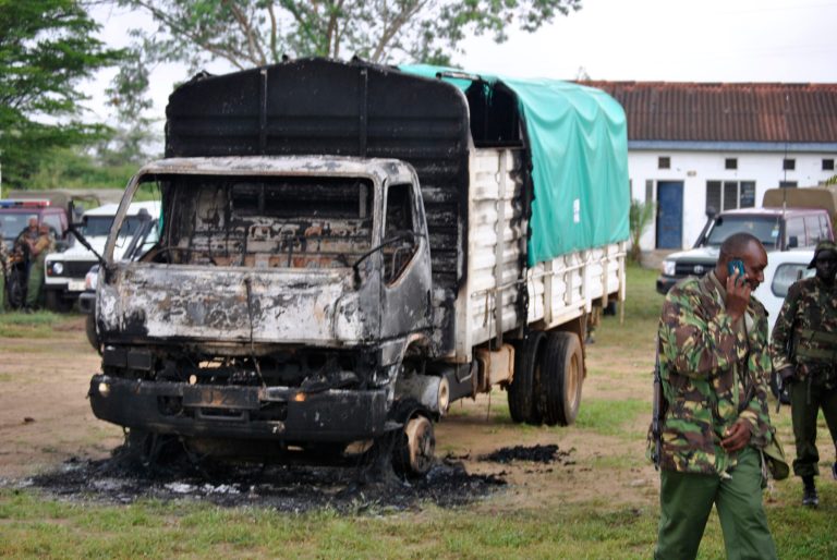 Policemen stand near the wreckage of a burnt vehicle after gunmen attacked, outside Gamba police station in Gamba, Kenya, Sunday, July 6, 2014. Eighteen people were killed in overnight attacks by the gunmen in two counties on the Kenyan coast, where last month al-Qaida-linked militants claimed responsibility for killing 65 people, the Kenya Red Cross said Sunday. The Sunday attacks took place in the towns of Hindi in Lamu county and Gamba in Tana River, the Kenya Red Cross chief Abbas Gulet said. Al-Qaida-linked al-Shabab militants from Somalia claimed responsibility for the attacks. (AP Photo)