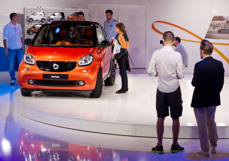 People stand beside the new Smart 'fortwo' during its world premiere in Berlin Wednesday, July 16, 2014. The new version is the same length at only 2.7 meters, or 8 feet, 10 inches, but is slightly wider and has a short front hood where the old one had none. (AP Photo/dpa, Soeren Stache)