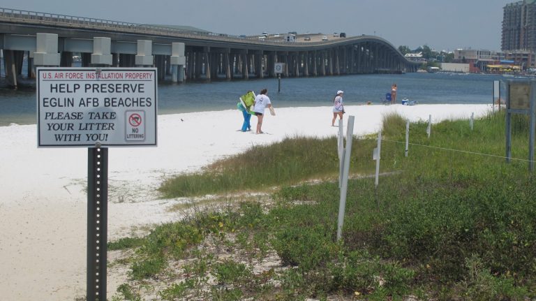 In this July 7, 2014 photo, people look for a place to set up on a shallow beach under a highway bridge in Destin, Fla. The beach is under the controlled of Eglin Air Force Base where it is occasionally used to practice amphibious landings and test high-tech weapons. The public is welcome to use the beach. (AP Photo/Melissa Nelson-Gabriel)