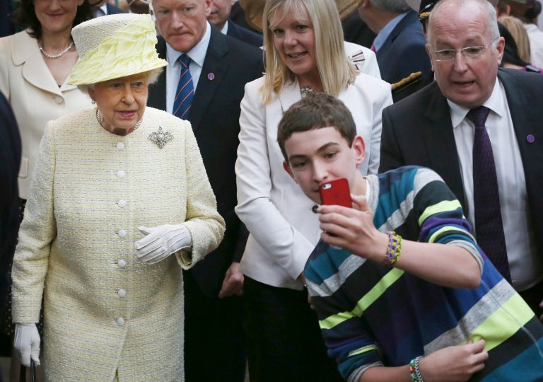 A local youth takes a selfie photograph in front of Queen Elizabeth II during a visit to St George's indoor market on  in Belfast Tuesday June 24, 2014. The Queen is on a 3 day visit to Northern Ireland .  (AP Photo/Peter Macdiarmid, Pool)