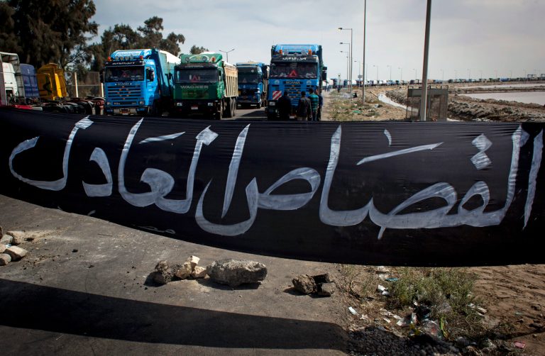 FILE - In this Friday, Feb. 22, 2013 file photo, Egyptian protesters, unseen, block a road preventing loaded trucks from leaving the port with a banner in Arabic that reads, 