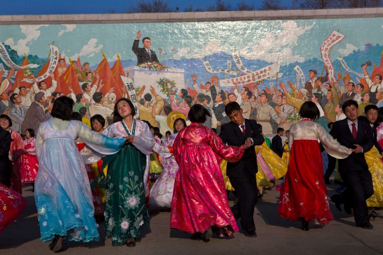 North Koreans dance together beneath a mosaic painting of the late leader Kim Il Sung during a mass folk dancing gathering in Pyongyang Thursday, April 11, 2013, to mark the anniversary of the first of many titles of power given to leader Kim Jong Un after the death of his father Kim Jong Il. (AP Photo/David Guttenfelder)