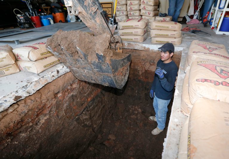 In this Thursday, May 1, 2014 photo, Jacob Ortiz, of Thunderground Storm Shelters, directs as the finishing touches are put on a hole for a storm shelter installation in the garage of a residence in Oklahoma City. Last year's deadly tornadoes, which killed more than 30 people, scared Oklahomans in a way that previous storms had not, moving them to add tornado shelters or reinforced safe rooms to their homes. In fact, surging demand has overwhelmed companies that build the shelters. (AP Photo/Sue Ogrocki)