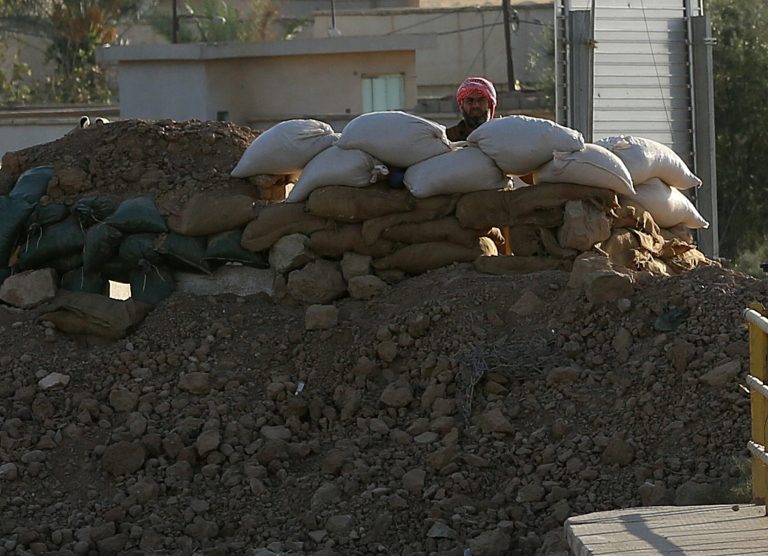 Militant with the Islamic State group peers from behind a barricade at a Kurdish peshmerga position near the Mullah Abdullah Bridge, located on the road between Irbil and Kirkuk, 290 kilometers (180 miles) north of Baghdad, Iraq, Saturday, Sept. 27, 2014. Over a wall of dirt bags across the Mullah Abdullah Bridge in northern Iraq, a militant with the Islamic State group looks at Kurdish fighters stationed on the other side of the bridge. (AP Photo/Hadi Mizban)