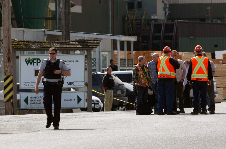 Mill workers talk as a police officer walks away following a shooting at Western Forest Products in Nanaimo, British Columbia, Wednesday, April 30, 2014. Four people were shot Wednesday at the lumber mill, police said they arrived at the mill within minutes and arrested the suspect. (AP Photo/The Canadian Press, Chad Hipolito)
