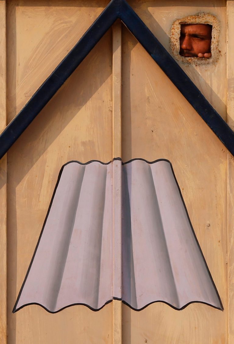 In this Nov. 23, 2013 photo, a guard looks out through a hole in the closed door of the Ramco Industries Ltd. factory which manufactures asbestos products in Bhojpur district of Bihar state, India. Scientists and medical experts overwhelmingly agree that inhaling any form of asbestos can lead to deadly diseases, but the Indian asbestos lobby say the risks are overblown. (AP Photo/Saurabh Das)