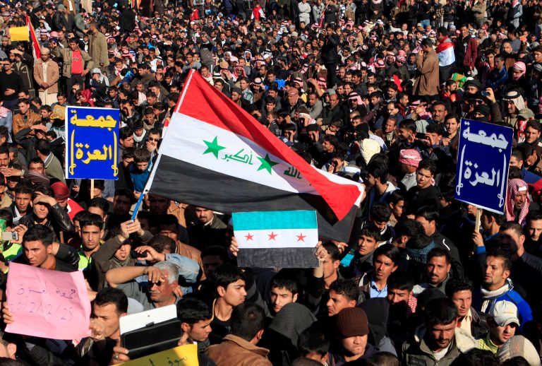   Protesters chant slogans against Iraq's Shiite-led government as they wave a national flag and a Syrian revolution flag during a demonstration in Fallujah, 40 miles (65 kilometers) west of Baghdad, Iraq, Friday, Dec. 28, 2012. Thousands of Iraqi Sunnis massed along a major western highway and in other parts of the country Friday for what appear to be the largest protests yet in a week of demonstrations, intensifying pressure on the Shiite-led government. The blue placards in Arabic read, 
