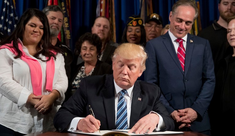 President Donald Trump, accompanied by Veterans Affairs Secretary David Shulkin, center right, and veterans, signs an Executive Order on 
