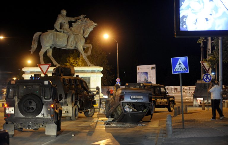 In this picture taken late Monday, May, 19, 2014, riot police vehicles pass by an overturned car on a street,  in Skopje, Macedonia. Police said Tuesday that 18 people were detained in a protest that turned violent late on Monday, after the murder of a 18-years old teenager in a western suburb of Macedonian capital Skopje. One man has been arrested in connection with the murder. (AP Photo/Boris Grdanoski)