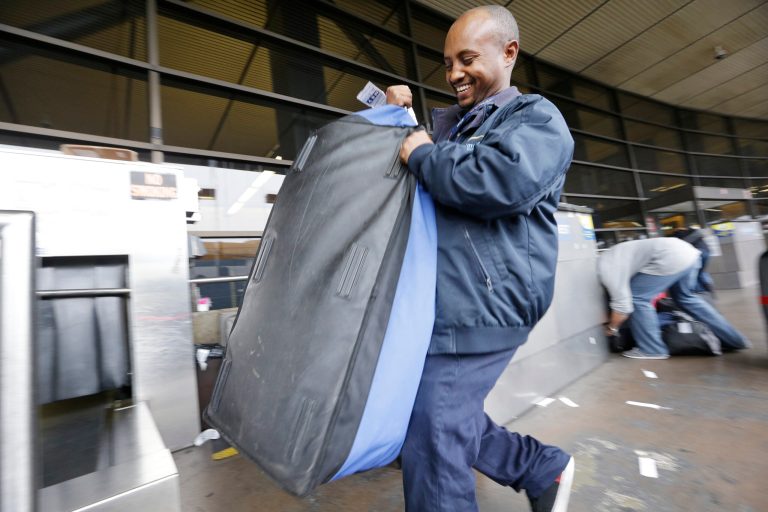 In this Tuesday, Oct. 22, 2013 photo, skycap Biniyam Yehuala hefts a traveler's bag at Seattle-Tacoma International Airport in SeaTac, Wash. A campaign to set a $15 minimum wage in the city of SeaTac is poised for victory. (AP Photo/Elaine Thompson)