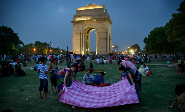 In this Wednesday, June 25, 2014 photo, a family spreads a sheet as they prepare to enjoy an evening at the lawns of India Gate park in New Delhi, India. With temperatures reaching 100 degrees every day, India Gate, the colonial park in the center of New Delhi is a temperate escape for the middle-class and working-class - the kind of people who don't have their own backyards, and can't afford air-conditioners and generators during power blackouts. It's a safe place for families to gather, to picnic, to buy balloons and pink cotton candy and watch dancing monkeys. (AP Photo/Saurabh Das)