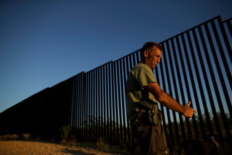 In this May 10, 2016 picture, Tim Foley gestures as he stands along the border wall separating Mexico and the United States in Sasabe, Ariz. Foley, a former construction foreman, founded Arizona Border Recon, a group of armed volunteers who dedicate themselves to border surveillance. (AP Photo/Gregory Bull)