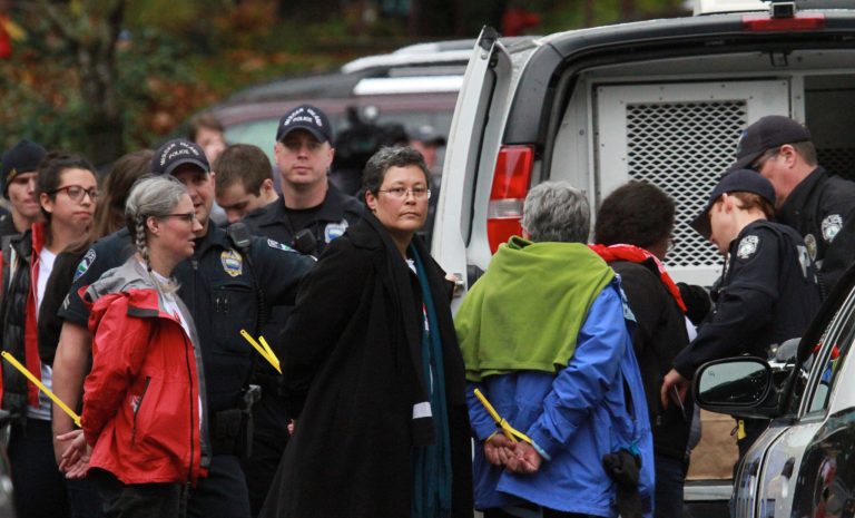 Peggy Lynch, center, facing camera, wife of outgoing Seattle mayor Mike McGinn, is handcuffed and waits to be loaded into Bellevue Police van after her arrest with other immigration reform protesters, Thursday, Nov. 7, 2013, at Washington State Republican Party Headquarters in Bellevue.  (AP Photo/The Seattle Times, Ken Lambert) 