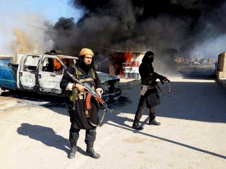 FILE - This undated file image posted on a militant website on Jan. 4, 2014, which is consistent with other AP reporting, shows Shakir Waheib, a senior member of the al-Qaida breakaway group Islamic State of Iraq and the Levant (ISIL), left, next to a burning police vehicle in Iraq's Anbar Province. For the al-Qaida breakaway group that overran parts of Iraq this week, the border between that country and Syria, where it is also fighting, may as well not even be there. The group, wants to establish a Shariah-ruled mini-state bridging both countries, in effect uniting a Sunni heartland across the center of the Mideast. (AP Photo via Militant Website, File)