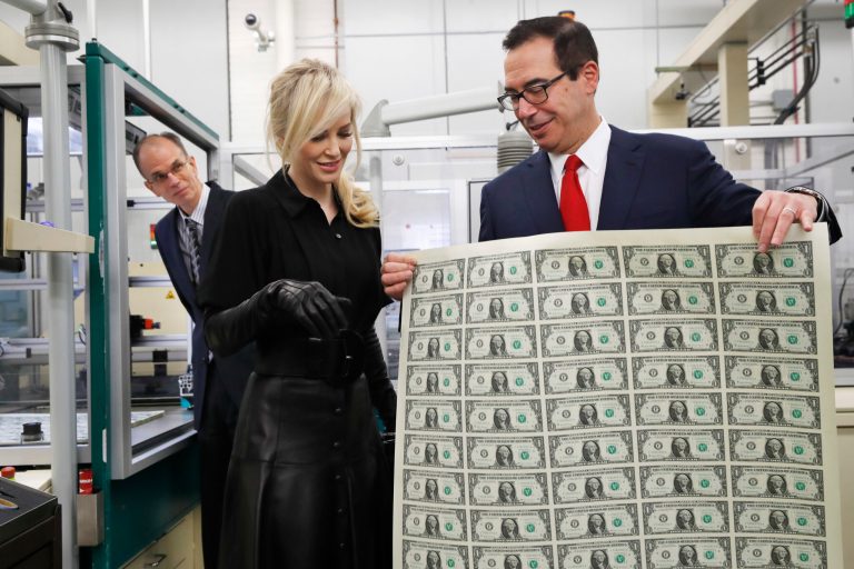 Treasury Secretary Steven Mnuchin, right, shows his wife Louise Linton a sheet of new $1 bills, the first currency notes bearing his and U.S. Treasurer Jovita Carranza's signatures, Wednesday, Nov. 15, 2017, at the Bureau of Engraving and Printing in Washington. The Mnuchin-Carranza notes, which are a new series of 2017, 50-subject $1 notes, will be sent to the Federal Reserve to issue into circulation. At left is BEP Director Leonard Olijar. (AP Photo/Jacquelyn Martin)
