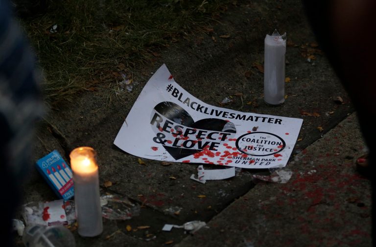 A sign and candle are seen at the location where Sylville Smith was shot and killed by Milwaukee police in Milwaukee, Sunday, Aug. 14, 2016. Police in Milwaukee say a black man whose killing by police on Saturday touched off arson and rock-throwing was shot by a black officer after turning toward him with a gun in his hand. Wisconsin's governor, meanwhile, has put the National Guard on standby in case of more violence Sunday night. (AP Photo/Jeffrey Phelps)