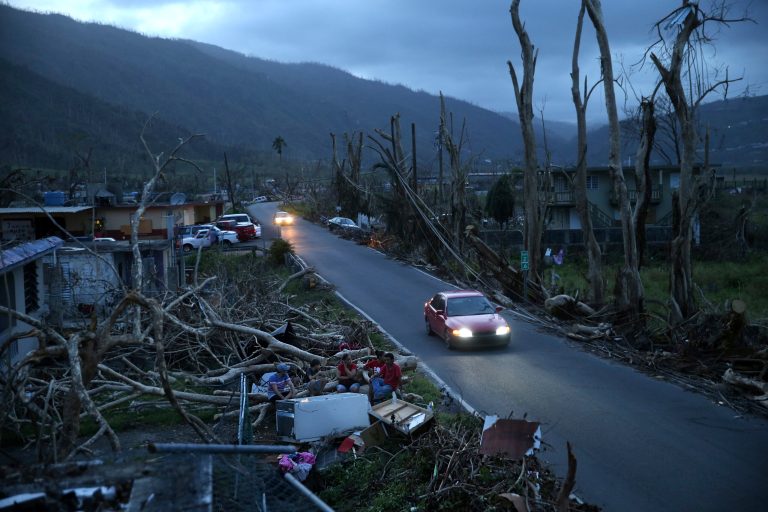 In this Sept. 26, 2017 photo, neighbors sit on a couch outside their destroyed homes as sun sets in the aftermath of Hurricane Maria, in Yabucoa, Puerto Rico. For decades AP journalists have worked in challenging conditions covering news around the world, but rarely have they had to navigate such constant shortages, blackouts and communications outages on U.S. soil. (AP Photo/Gerald Herbert)