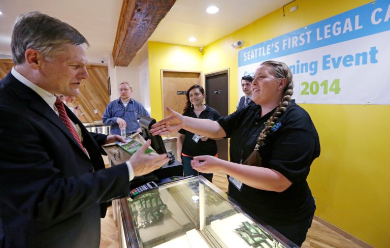 Seattle City Attorney Pete Holmes, left, shakes hands with clerk Pam Fenstermacher after purchasing marijuana at Cannabis City, Tuesday, July 8, 2014, in Seattle, on the first day that sales of recreational pot became legal in the state.  Washington on Tuesday became the second state to allow people to buy marijuana legally in the U.S. without a doctor's note as eager customers who lined up outside stores made their purchases and savored the moment. (AP Photo/Elaine Thompson, Pool)