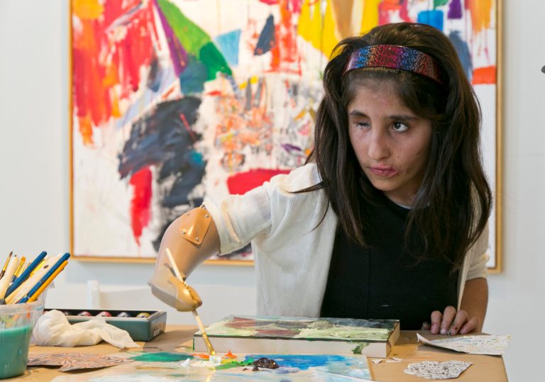 Afghan war victim Shah Bibi Tarakhail uses her new prosthetic arm to paint during a private session with artist Dayvd Whaley at Galerie Michael in Beverly Hills, Calif., Wednesday, April 2, 2014. Shah Bibi, a 7-year-old Afghani who lost her arm after picking up a grenade, received a new prosthetic arm at Shriners Hospital for Children and will be heading back home to her family on April 8, though she will return to Southern California in coming summers for additional medical procedures, including receiving a prosthetic eye. (AP Photo/Damian Dovarganes)