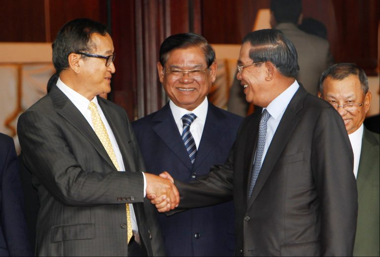 Cambodian Prime Minister Hun Sen, right, shakes hands with the main opposition party leader Sam Rainsy, left, of Cambodia National Rescue Party, as Deputy Prime Minister Sar Kheng, center, smiles after their meeting in Senate headquarters in Phnom Penh, Cambodia, Tuesday, July 22, 2012. Hun Sen and opposition leader Rainsy said Tuesday that they had agreed upon a joint political solution to end the crisis. (AP Photo/Heng Sinith)