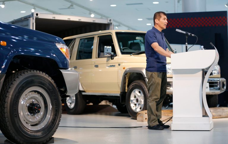 Toyota Land Cruiser chief engineer  Sadayoshi Koyari speaks in front of the Land Cruiser 70 van, right, and its pickup model, left, during the Land Cruiser Motor Show at a Toyota showroom in Tokyo Monday, Aug. 25, 2014. Toyota Motor Corp. is bringing back the Land Cruiser 70 in Japan, catering to nostalgic demand for the rugged off-road vehicle. The Land Cruiser 70, the toughest of the Land Cruiser models, arrives at Japanese dealers Monday. But it's on sale for only a year. (AP Photo/Shizuo Kambayashi)