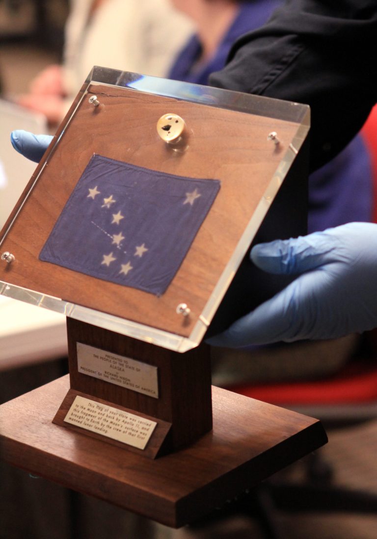   Alaska State Museum curator of collections Steve Henrikson shows a plaque containing an Alaska flag below moon rocks encased in acrylic glass on Thursday, Dec. 6, 2012, at Anchorage School District offices in Anchorage, Alaska. President Richard Nixon presented the display to Alaska Gov. Keith Miller in 1969 after the Apollo 11 moon mission. The display disappeared from a museum after an arson fire in 1973 but was returned to the state Wednesday after settlement of a lawsuit. (AP Photo/Dan Joling)  