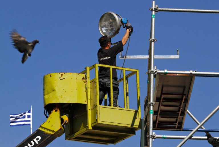   A pigeon flies next of a worker as he places a large light projector to prepared for a final election rally of the New Democracy party Friday night in front of the Parliament at Syntagma square in central Athens, Thursday, June 14, 2012. Greece faces crucial national elections on Sunday, that could ultimately determine whether the debt-saddled, recession bound country remains in the eurozone. (AP Photo/Petros Karadjias)  