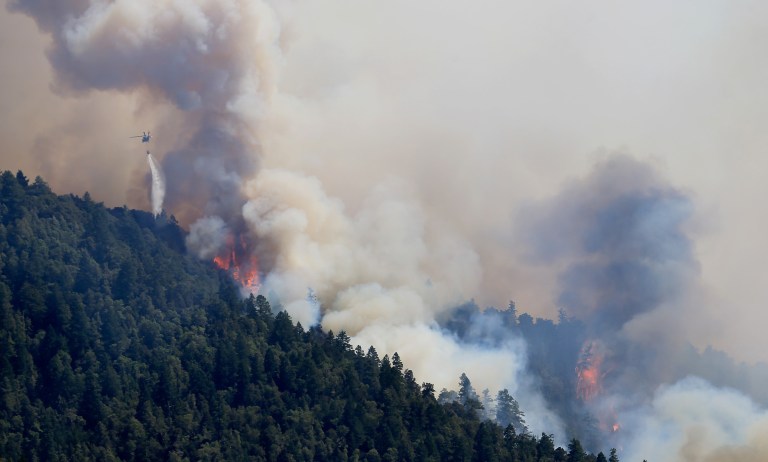 An Air National Guard helicopter makes a water drop as the Lodge Fire between Legget tand Laytonville, Calif., jumps the Eel River and moves upslope, Friday Aug. 8, 2014.  The fire was started by lightning on July 30 and has grown to 5,400 acres.   (AP PhotoThe Press Democrat, Kent Porter)