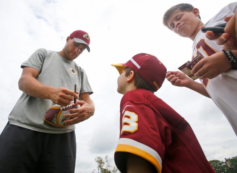 Washington Redskins quarterback Kirk Cousins (8) signs a football for young fans after the morning practice at the Redskins NFL football teams training camp in Richmond, Va., Friday, July 29, 2016. (AP Photo/Steve Helber)