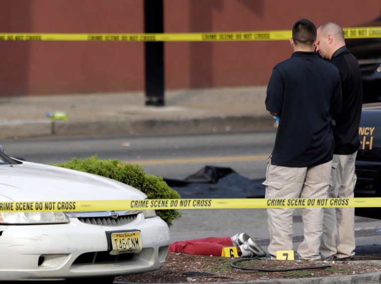 A person lays on the ground near evidence markers as officials investigate the scene where a Jersey City Police Department officer was shot and killed while responding to a call at a 24-hour pharmacy, Sunday, July 13, 2014, in Jersey City, N.J.  Officer Melvin Santiago was shot in the head while still in his police vehicle as he and his partner responded to an armed robbery call  at about 4.a.m., Jersey City Mayor Steven Fulop said in a statement.  Fulop said officers responding to the robbery call shot and killed the man who shot Santiago. He was not immediately identified.(AP Photo/Julio Cortez)