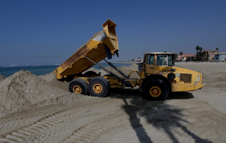 Dump trucks work to pile sand on a temporary berm to protect beach front homes on, Friday, Sept. 5, 2014, in Long Beach, Calif. Southern California is in for another round of high surf generated by what is currently Hurricane Norbert in the Pacific Ocean off Baja California. (AP Photo/Chris Carlson)