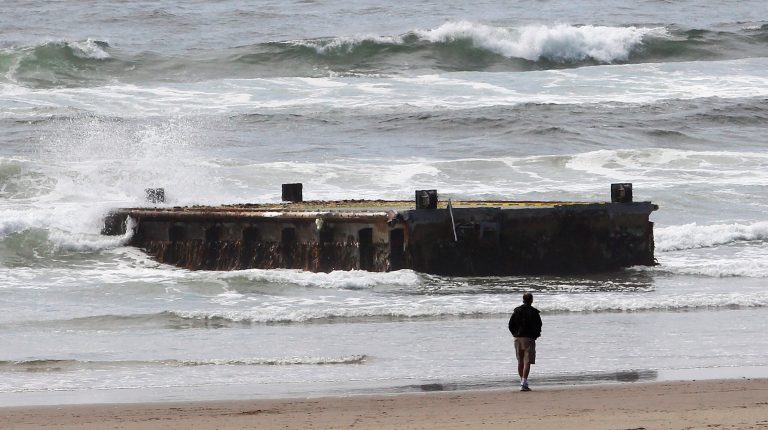   FILE -In this file photo from Wednesday, June 6, 2012, a man looks at a 70-foot-long dock with Japanese lettering that washed ashore on Agate Beach in Newport, Ore. The West Coast is anticipating more debris from the 2011 Japanese tsunami to wash ashore this winter. Scientists expect the bulk of the tsunami debris to end up in the Pacific Northwest. (AP Photo/Rick Bowmer, File)  
