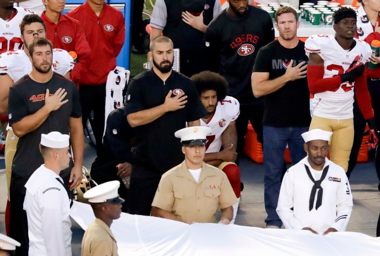 In this Sept. 1, 2016, photo, San Francisco 49ers quarterback Colin Kaepernick, center, kneels during the National Anthem before an NFL preseason football game against the San Diego Chargers in San Diego. What started as a protest against police brutality has mushroomed a year later into a divisive debate. (AP Photo/Chris Carlsone)