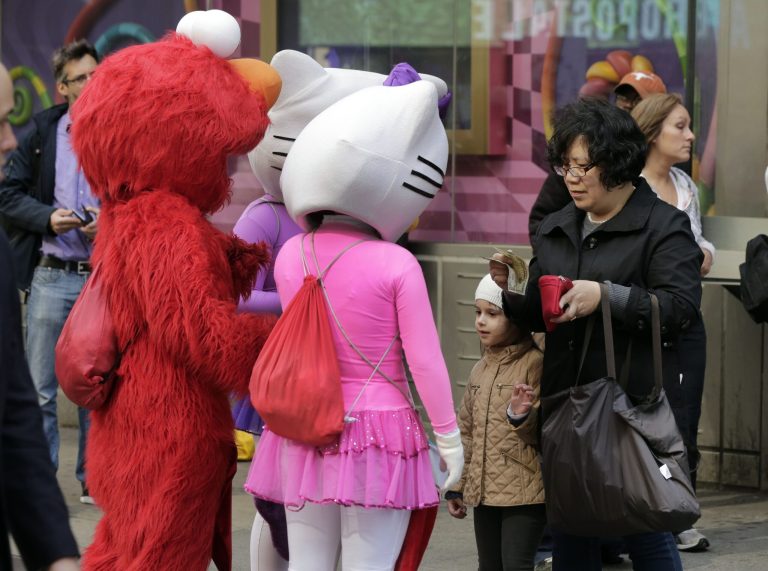 A woman gives a monetary tip to characters in New York's Times Square after she photographed the girl with them, Tuesday, April 9, 2013. A string of arrests in the last few months has brought unwelcome attention to the growing number of people, mostly poor immigrants, who make a living by donning character outfits, roaming Times Square and charging tourists a few dollars to pose with them in photos. (AP Photo/Richard Drew)