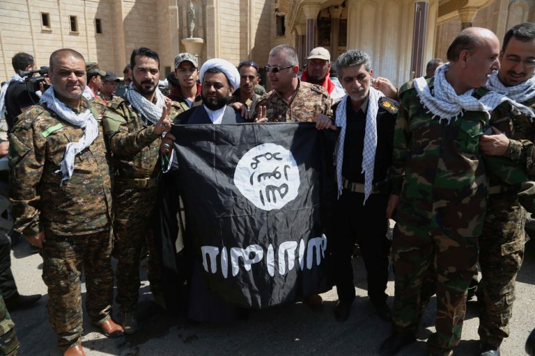 Members of the Iraqi security forces and clerics pose for a photo with the Islamic State group flag after they took it down at one of Saddam Hussein's palaces in Tikrit, 80 miles (130 kilometers) north of Baghdad, Iraq, Thursday, April 2, 2015, a day after Iraqi security forces backed by Shiite militiamen took control of the city from Islamic State militants. (AP Photo/Khalid Mohammed)