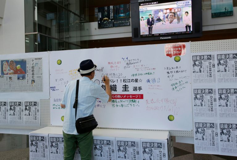 A man writes a message to Japanese tennis player Kei Nishikori on a board with newspapers reporting him in the U.S. Open, in Nishikori's hometown of Matsue, western Japan, Monday, Sept. 8, 2014. Nishikori, the first man from Asia to make it to the final of a Grand Slam singles tournament, faces Marin Cilic in the U.S. Open men's final on Monday. The newspapers' headlines read: 