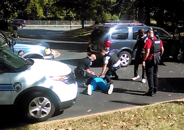Charlotte police squat next to Keith Lamont Scott as Scott lies face-down on the ground, in Charlotte, N.C. The video does not show clearly whether Scott had a gun. (Rakeyia Scott/Curry Law Firm via AP)