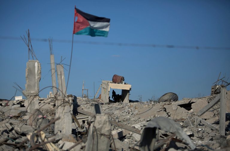 In this Wednesday, Oct. 1, 2014 photo, a Palestinian flag waves as a man walks over the rubble of houses that were destroyed in the recent Israel-Hamas war, in Khuzaa, southern Gaza Strip. More than five weeks after the war in the Gaza Strip, tens of thousands of people whose homes were destroyed or badly damaged in the fighting still live in classrooms, storefronts and other crowded shelters. Yet despite their pressing needs, reconstruction efforts appear stymied by a continued Israeli-Egyptian border blockade of Gaza and an unresolved power struggle between the Islamic militant group Hamas and Western-backed Palestinian President Mahmoud Abbas. (AP Photo/Khalil Hamra)