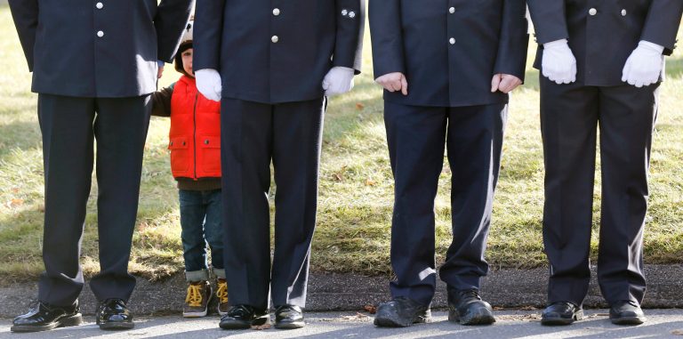   A child peers through firefighters standing as the procession heads to the cemetery outside the funeral for school shooting victim Daniel Gerard Barden at St. Rose of Lima Catholic Church in Newtown, Conn., Wednesday, Dec. 19, 2012. According to firefighters, Daniel wanted to be a firefighter when he grew up and they honored him at the service. Barden, 7, was killed when Adam Lanza walked into Sandy Hook Elementary School in Newtown, Conn., Dec. 14, and opened fire, killing 26 people, including 20 children, before killing himself. (AP Photo/Charles Krupa)  