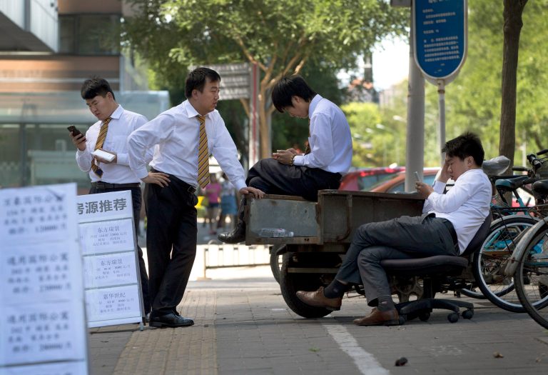 In this Saturday, June 7, 2014 photo, real estate sales agents check on their smartphones near display boards show properties for sale and rent, as they wait for potential buyers in Beijing, China. Reality has arrived in Chinaâs housing market. Prices that soared out of reach for families are cooling under pressure from government lending curbs. That has sparked concern about the impact on Chinaâs banks and economy. But Chinese leaders appear willing to let investors suffer losses to defuse tensions over lack of affordable housing. (AP Photo/Andy Wong)