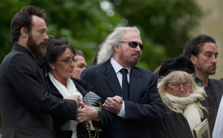   Barry Gibb, center, and Robin Gibb's wife Dwina Gibb, right, who holds an order of service, react at the graveside during the burial of Robin Gibb outside St Mary's Church in Thame, England, Friday, June 8, 2012. Robin Gibb a member of the iconic Bee Gees pop group died May 20, after a long battle with cancer.(AP Photo/Alastair Grant)  