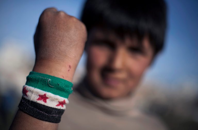 In Saturday, April 5, 2014 photo, Ahmed Mahmoud, 12, shows his wrist band with colors of the Syrian revolution flag, near his family's makeshift tent in an unofficial Syrian refugee camp on the outskirts of Amman, Jordan. For Ahmed, school is a distant memory. He helps his father sell vegetables in a wholesale market near their camp where he has lived the past year.(AP Photo/Khalil Hamra)