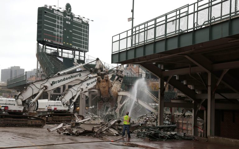 Workers use hoses to keep dust down as construction equipment starts to take big bites out of Wrigley Field's outfield walls. Thursday, Oct. 16, 2014, in Chicago. The demolition of the historic ballpark's famous bleachers is part of a project to build a large electronic sign and six other outfield signs. The work is part of the Cubs' privately funded $575 million renovation project. (AP Photo/M. Spencer Green)