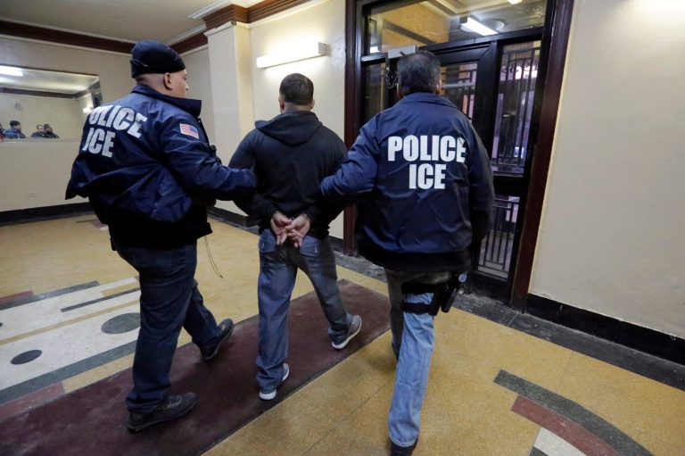 Immigration and Customs Enforcement officers escort an arrestee in an apartment building. (AP Photo/Richard Drew)