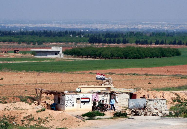 Syrian soldiers at a Syrian army post as seen from the Lebanese border village of al-Qasr, Lebanon, Friday, April 12, 2013. Syrian warplanes and troops battled rebels near the border with Lebanon as part of a widening government counteroffensive to recapture territory along strategic border areas and near the capital Damascus. Written on the army post are the words 