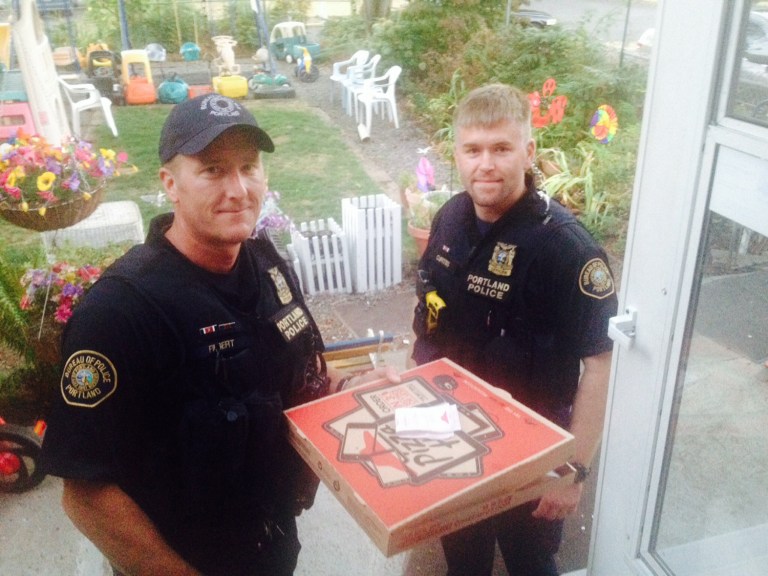 In this photo taken Sept. 1, 2014, and provided by Steve Huckins, Portland police officers Michael Filbert, left, and Royce Curtiss, right, pose after completing a pizza delivery to the Huckins home after a Pizza Hut delivery driver was hurt in a crash in Portland, Ore.  Huckins and his wife were concerned when the officers showed up at their home, but they started laughing when they received the pizza. They're thanking the officers for going out of their way. The driver hurt his neck and back in the collision at an intersection, but is now okay. (AP Photo/Steve Huckins)