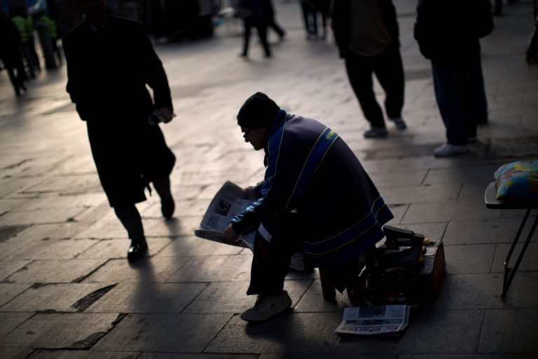   A shoeshine reads a newspaper as he waits for customers in a street in Madrid, Tuesday, Dec. 4, 2012. The number of people officially registered as unemployed in Spain has edged up toward 5 million as the country's recession shows few signs of abating and its struggling banks await crucial bailout cash, Spain's Labor Ministry said Tuesday. (AP Photo/Emilio Morenatti)  